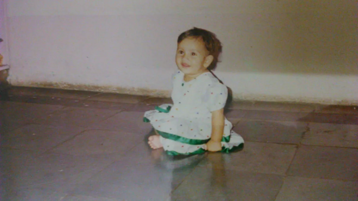 Apoorva as a baby, in a white dress with green ribbon